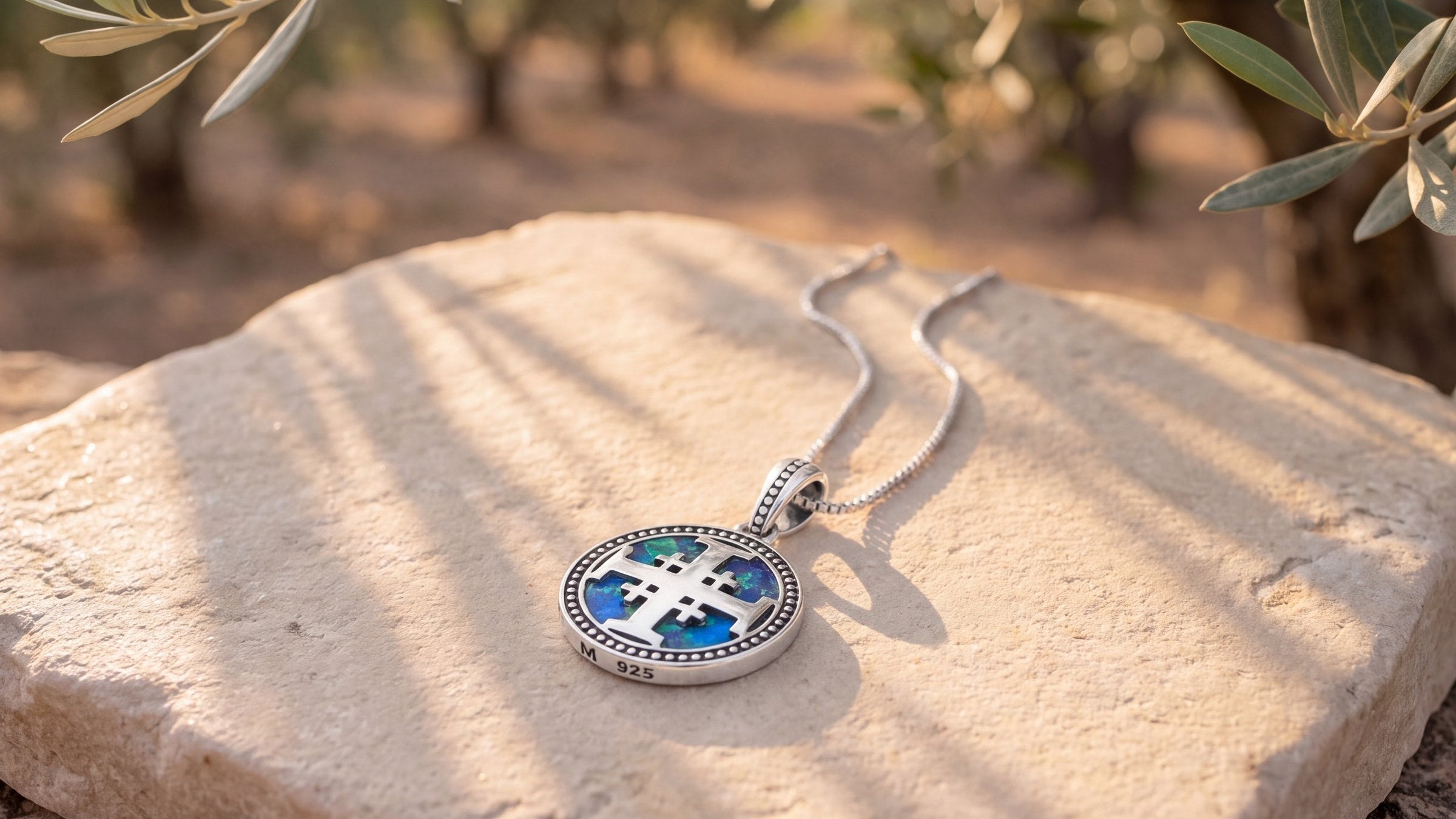 Jerusalem Cross Eilat Stone disc pendant necklace lying on a limestone slab in an olive grove