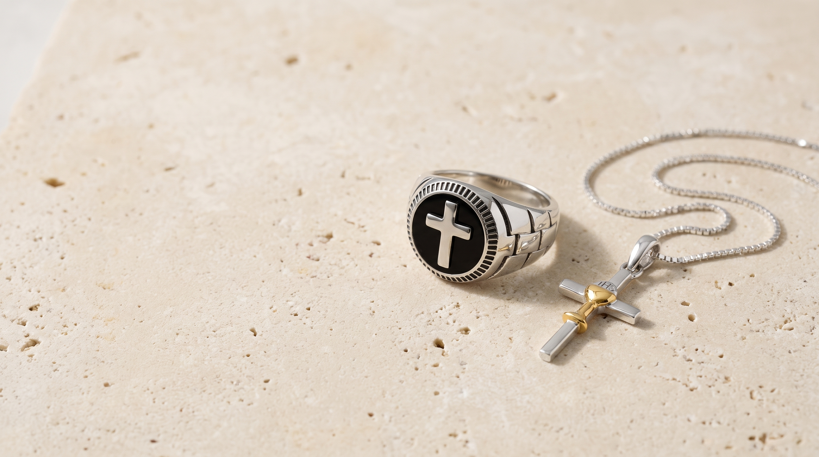 Men's onyx cross signet ring and chalice cross pendant on pale limestone, desktop banner