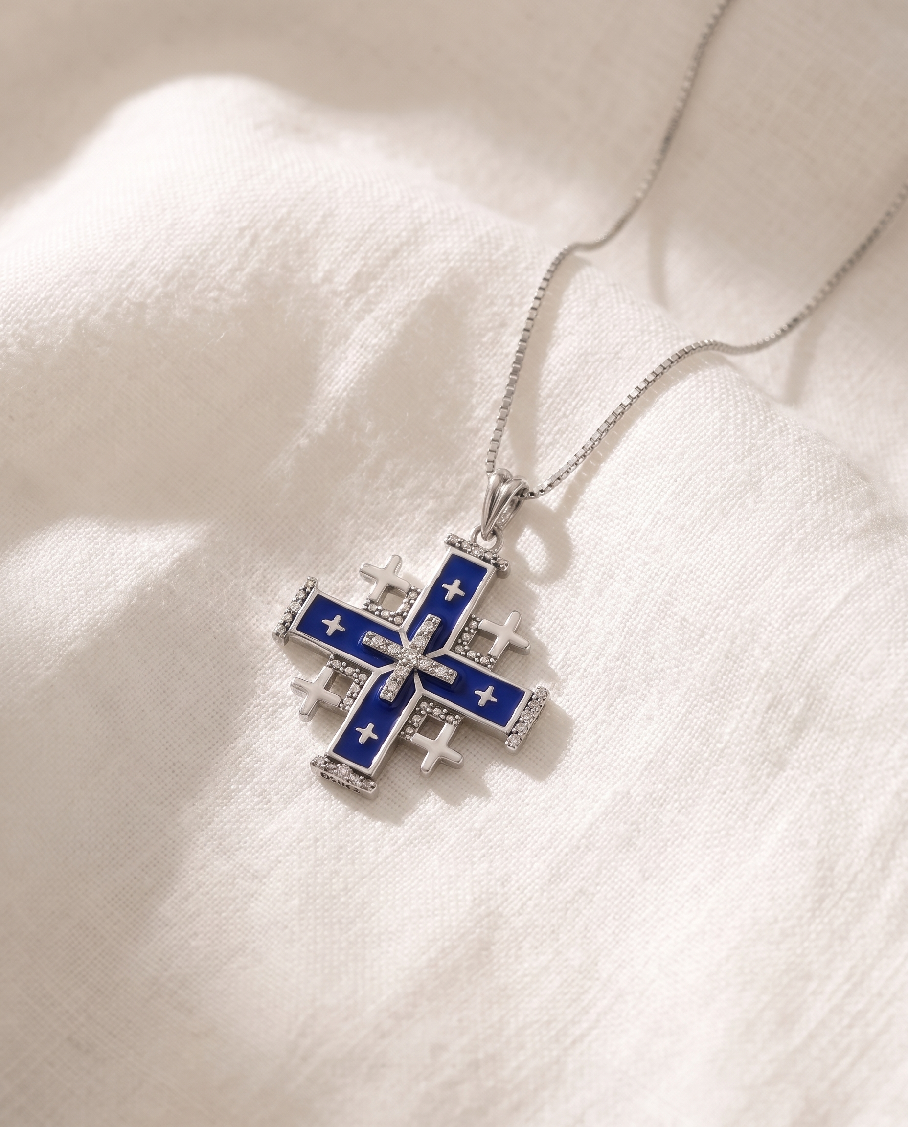 Blue enamel Jerusalem Cross pendant necklace on white fabric